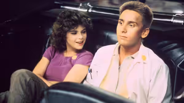 Otto Maddox (Emilio Estevez) sits beside a woman in the backseat