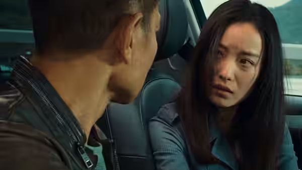A woman speaks anxiously to a man in a leather jacket inside a car