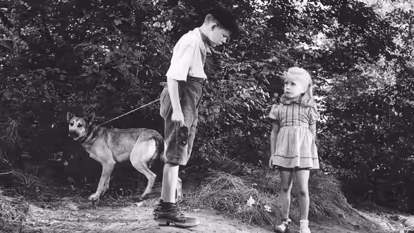 Michel Dolle (Georges Poujouly) and Paulette (Brigitte Fossey) stand with a dog beside the woods