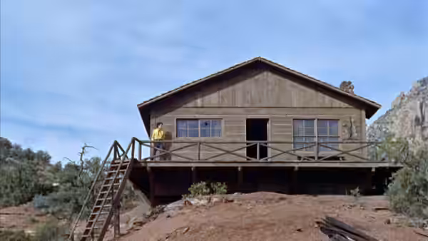 A raised wooden building with a long balcony stands amid rocky countryside