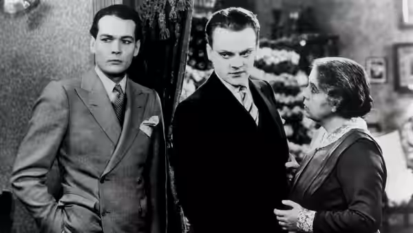 Two suited men stand beside an older woman in a furnished room