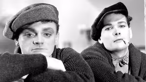 Two young men in flat caps sit close together and look ahead