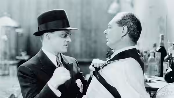 Two suited men face each other indoors, one gripping his lapel