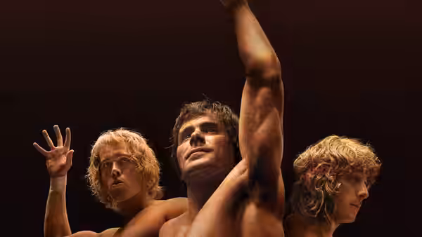Three shirtless wrestlers stand together, one raising his arm high