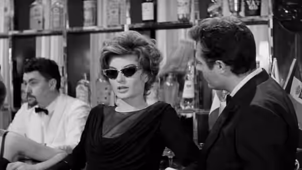 Maddalena (Anouk Aimée) in sunglasses sits at a bar beside Marcello Rubini (Marcello Mastroianni)