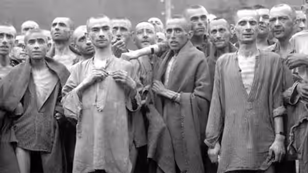Group of thin men in striped uniforms stand closely together outdoors