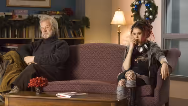 An older man and a young woman sit apart on a living room sofa