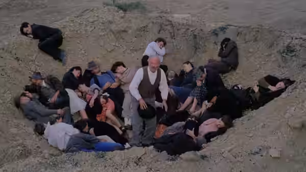 A man stands among villagers lying in a shallow crater