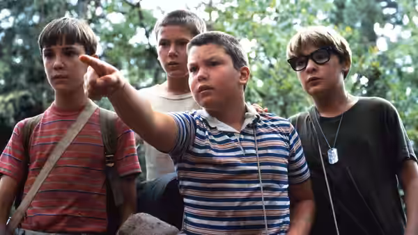 Four boys stand in woods one points forward while others look on