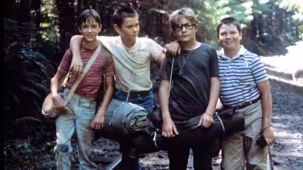 Four boys stand in forest carrying a rolled bundle on a pole