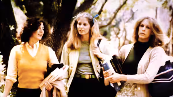 three young women stand together outdoors holding books and jackets