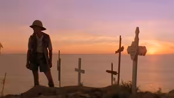 a man standing among wooden crosses overlooking the sea at sunset