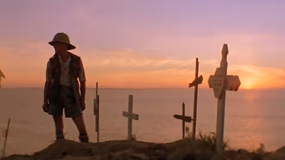 a man standing among wooden crosses overlooking the sea at sunset