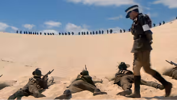 an officer walking past soldiers lying prone on a sandy slope