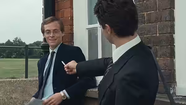 Dakin offers a cigarette to a bespectacled student beside the school building