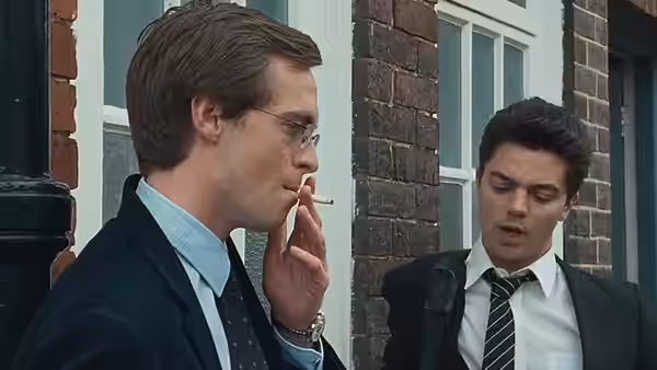 A bespectacled student smokes as Dakin talks beside the brick school wall