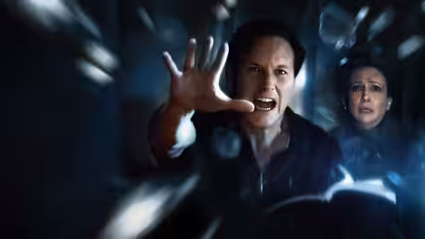 Ed Warren (Patrick Wilson) reaching forward with Lorraine Warren (Vera Farmiga) behind him