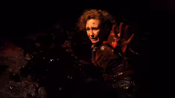 Blood-covered woman with curly hair reaching out her hand in darkness