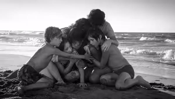 Group of children huddled together on the sand at the edge of the sea