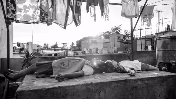 Two people lie on their backs on a concrete ledge under hanging laundry