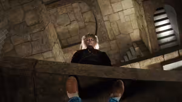 Jareth (David Bowie) seated on a stone ledge in the labyrinth