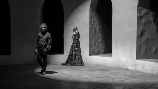 a man and a woman standing in an arched stone corridor