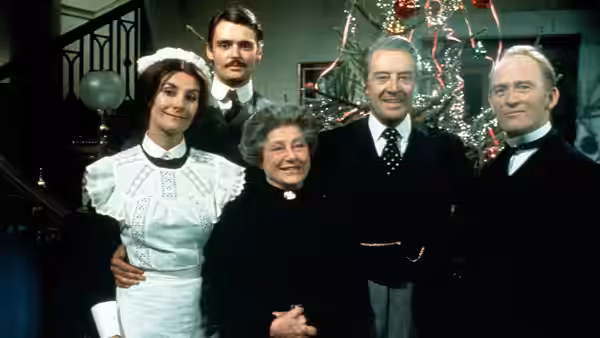 A maid and four others gathered together indoors near a Christmas tree