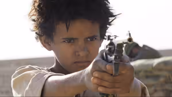 Theeb aims a pistol with both hands in the desert