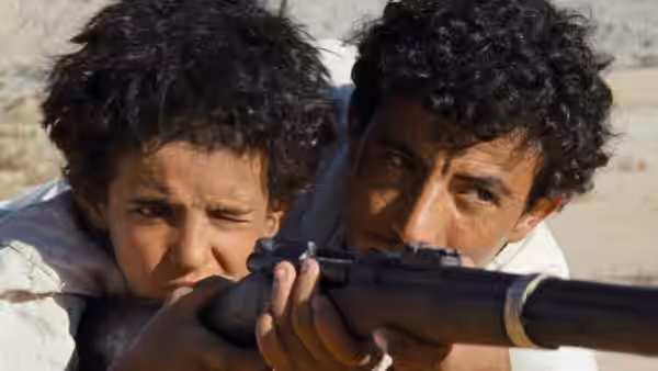 Hussein helps Theeb aim a rifle across the desert