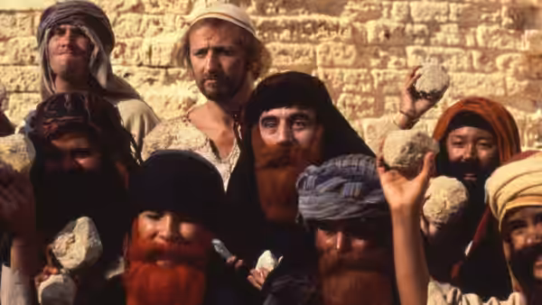 Crowd of bearded men in head coverings hold stones with raised hands
