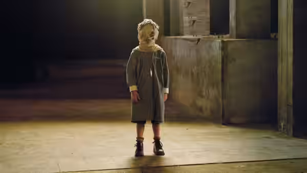 A young child stands alone in a dim, worn room