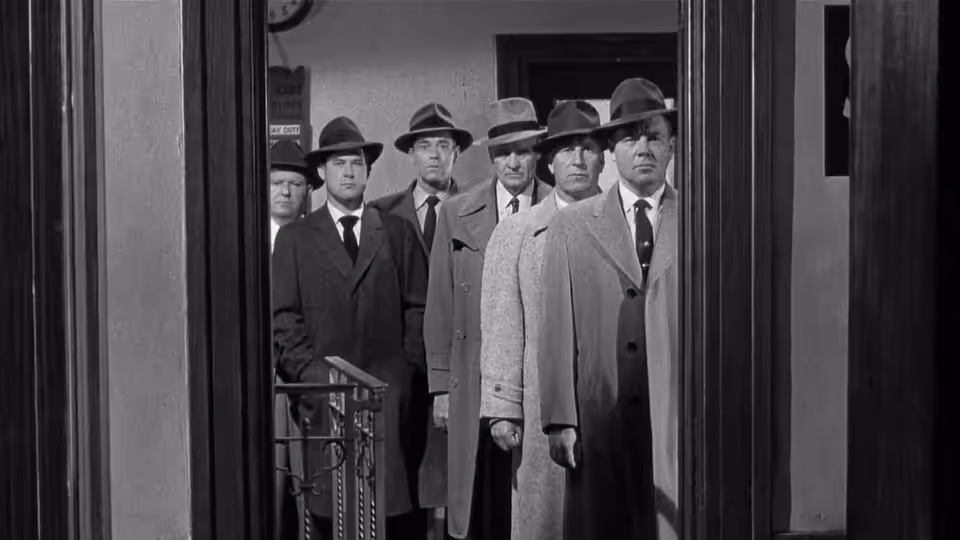 Five men in hats and suits stand in a row behind a partition