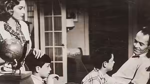 A woman stands beside a globe as two children face a seated man
