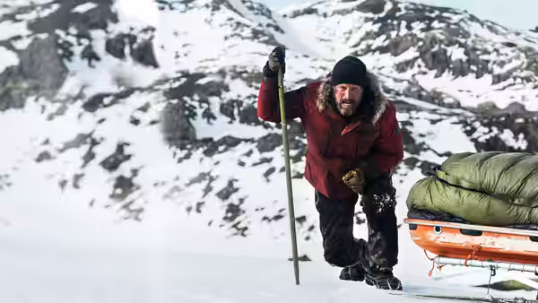 H. Overgård (Mads Mikkelsen) climbs snowy slopes, pulling a sled behind him