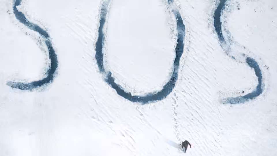 A lone figure crosses a vast snowfield marked with dark tracks