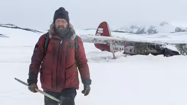H. Overgård (Mads Mikkelsen) walks past a crashed plane in the snow