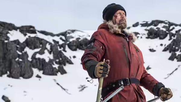 H. Overgård (Mads Mikkelsen) stands with a walking pole among snow-covered mountains