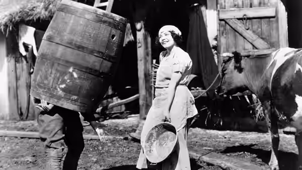 A smiling woman stands beside a horse-drawn wagon as a man carries a large crate