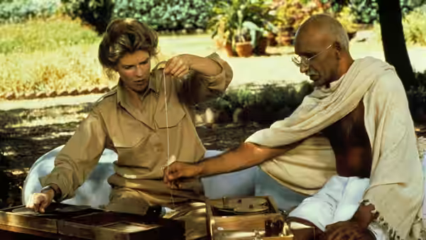 Gandhi (Ben Kingsley) and a man in khaki examine equipment outdoors