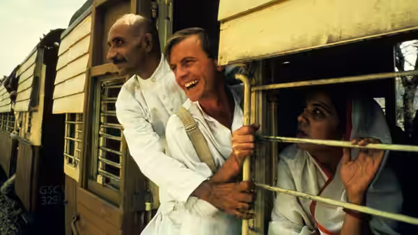Gandhi (Ben Kingsley) and a smiling man lean from a train window