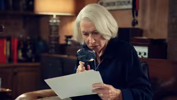 Elizabeth examining document closely with magnifying glass in study