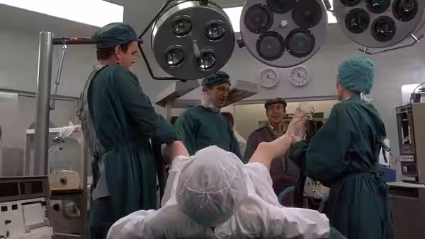 Surgeons in green scrubs attend to a patient on an operating table in a hospital