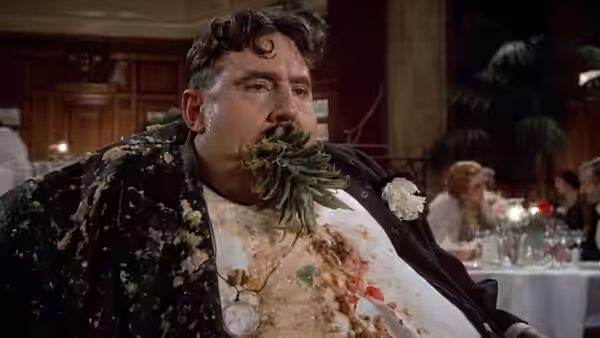 A disheveled man with food smeared on his face and clothes sits in a restaurant