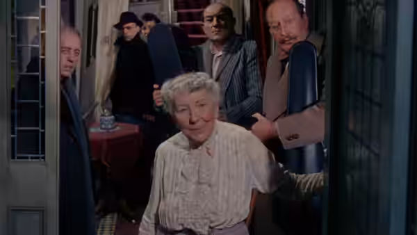 Mrs. Wilberforce (Katie Johnson) steps through a doorway as the gang crowd behind her