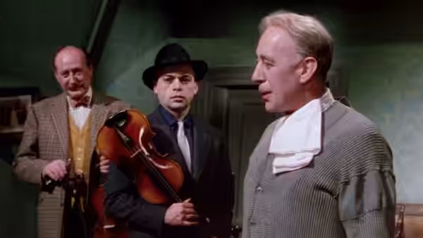 Professor Marcus (Alec Guinness) stands with his violin as two men watch in a room