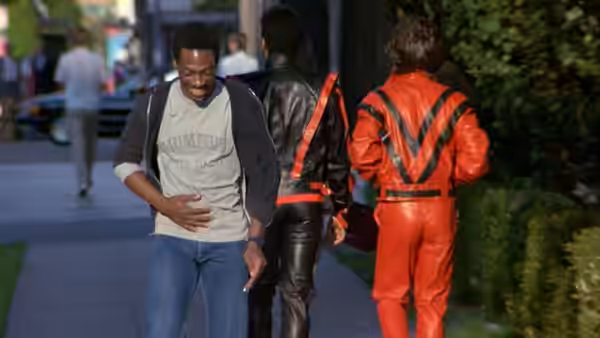 Axel Foley (Eddie Murphy) walking beside two men in leather outfits