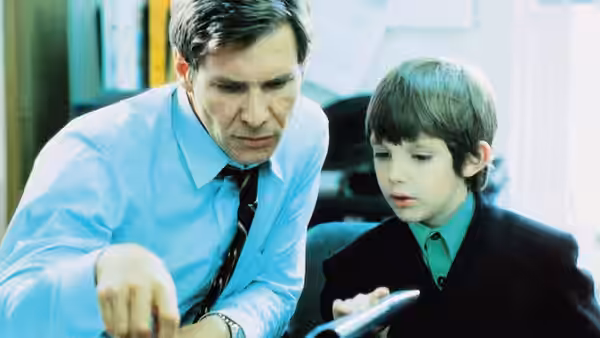 John Book (Harrison Ford) leans over a young boy examining an object together