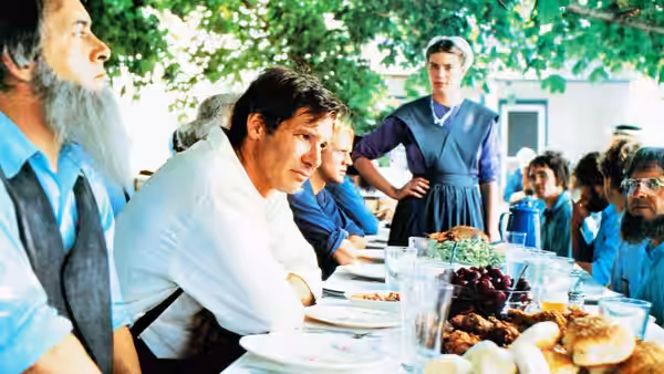 John Book (Harrison Ford) sits at a table during a communal outdoor meal