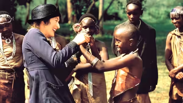 Karen Blixen (Meryl Streep) holding hands with a boy among onlookers outdoors