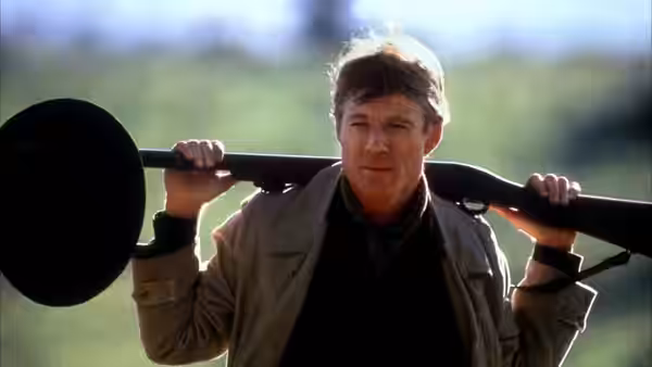 Denys Finch Hatton (Robert Redford) carrying a rifle across his shoulders outdoors